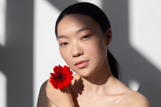 Radiant Asian woman holding a red flower against soft daylight shadows – embodying Seiya Skin’s poetic elegance and natural beauty ritual.